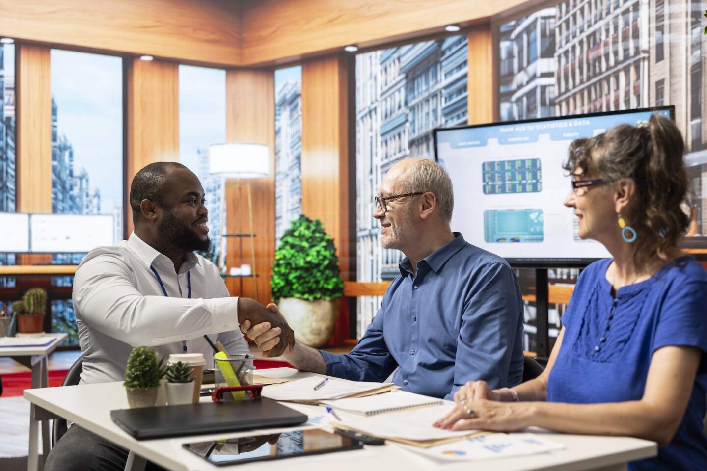 Financial adviser shaking hands in agreement with elderly man, ensuring a partnership to help them secure their pension and retirement planning. Meeting in modern office for counseling.
