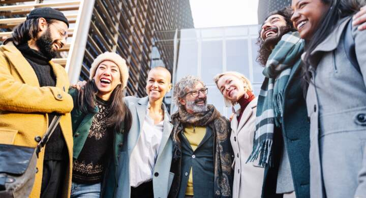 Happy team of professional business people embracing and laughing together outdoors. Cooperation and friends at work