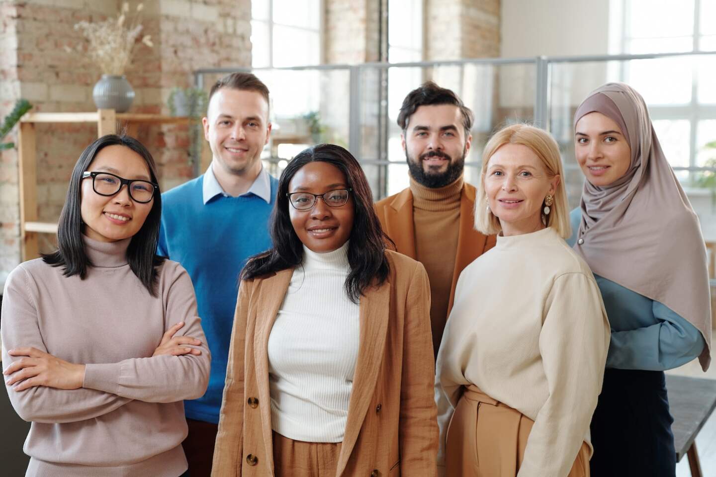 Group of smiling young interracial colleagues of modern company standing together in loft open space office