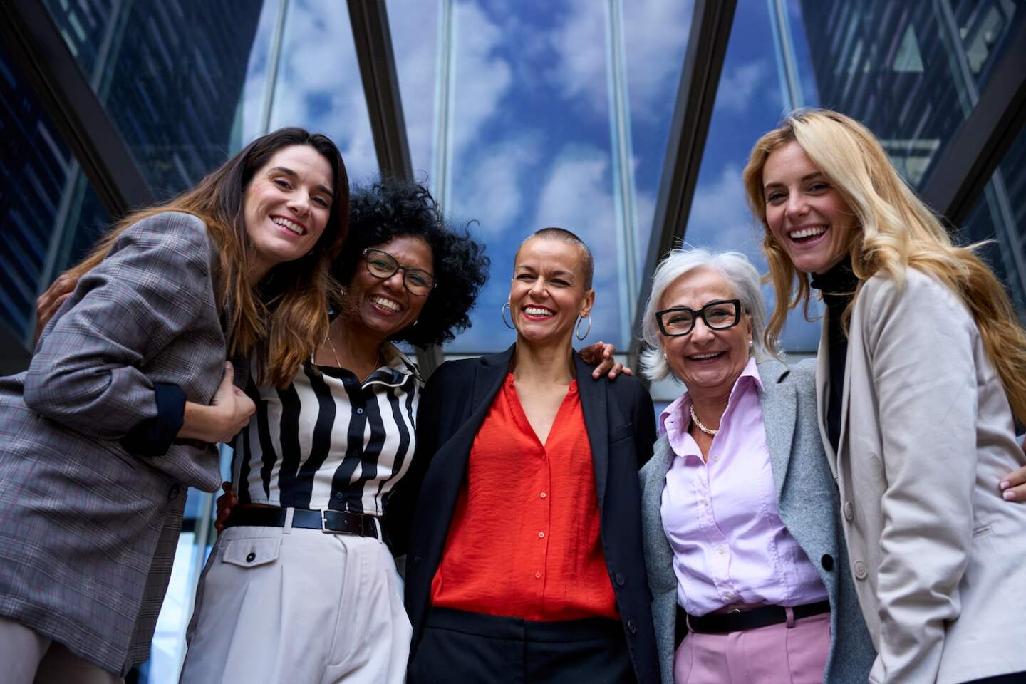 Female members of the middle-aged company team hugging together outside the office laughing and looking at the camera. Enjoying friendly relations between colleagues. Copy space