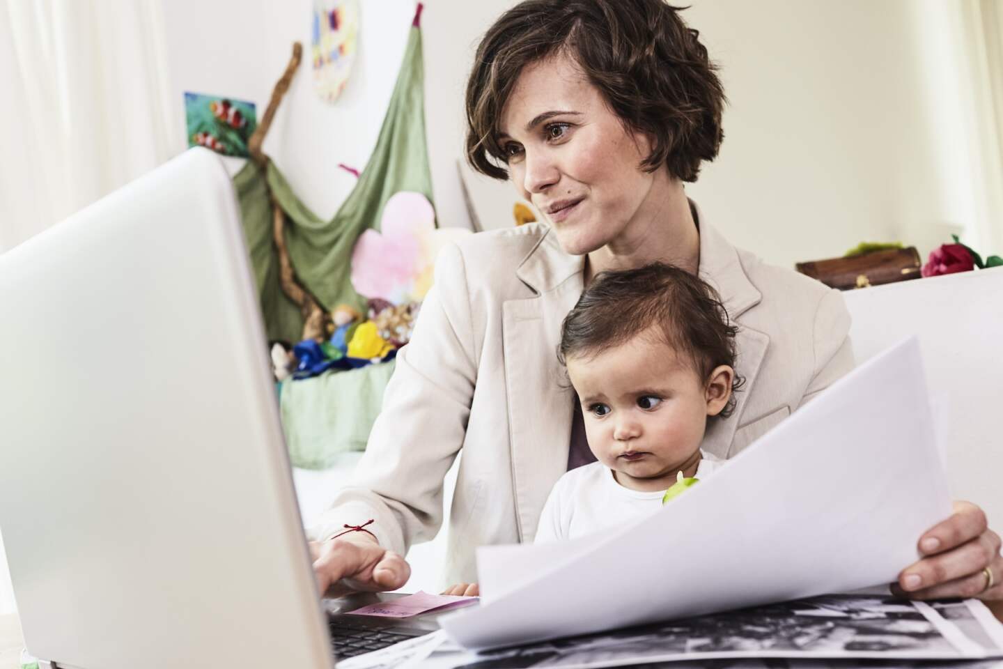 Mother holding sitting with baby daughter, working on laptop