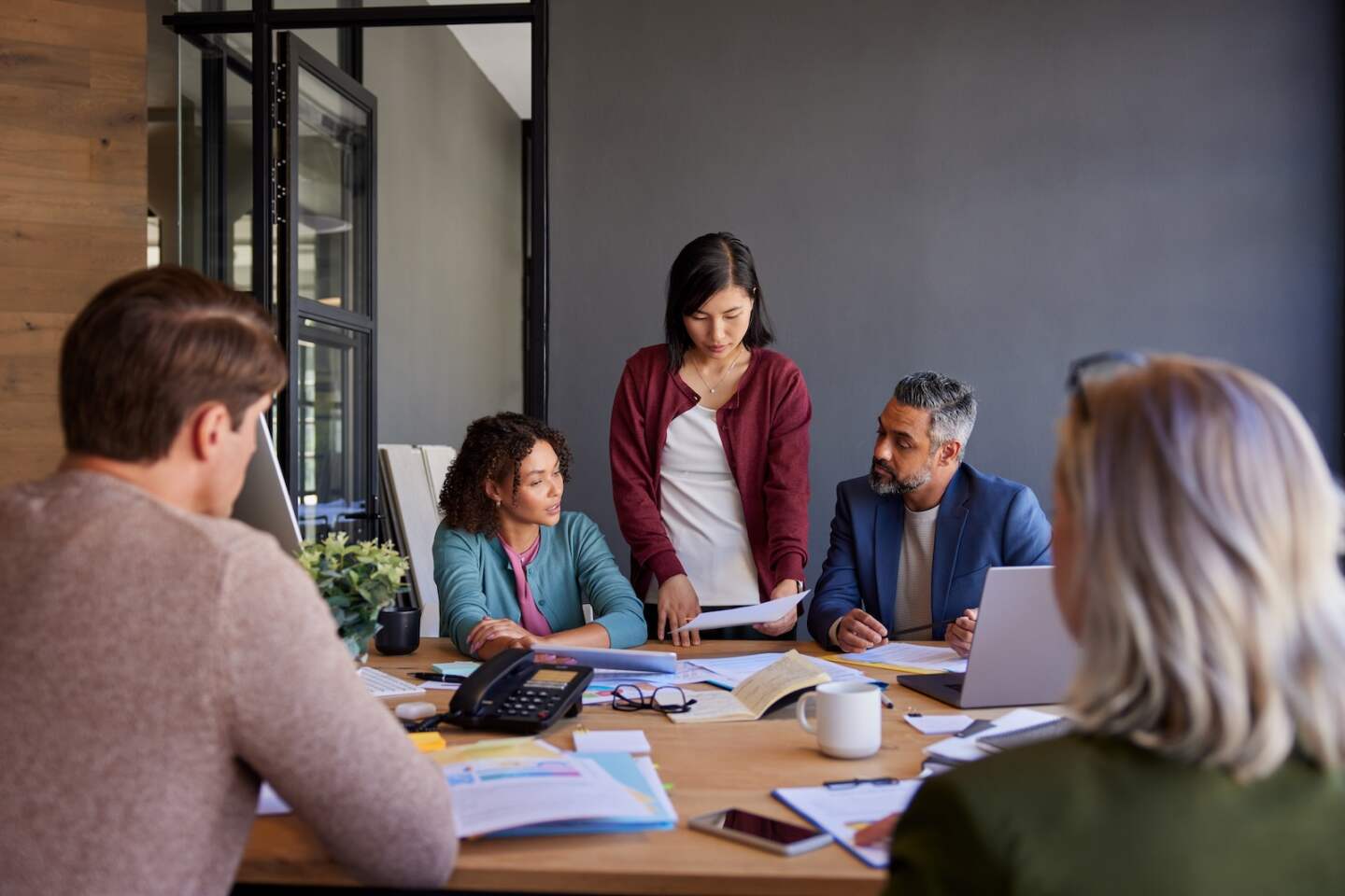 Group of multiethnic businesspeople discussing project details, focusing on data analysis and business growth. Engaged team members reviewing documents and sharing insights to drive the project forward. Asian woman showing business reports to her colleagues in a modern meeting room.