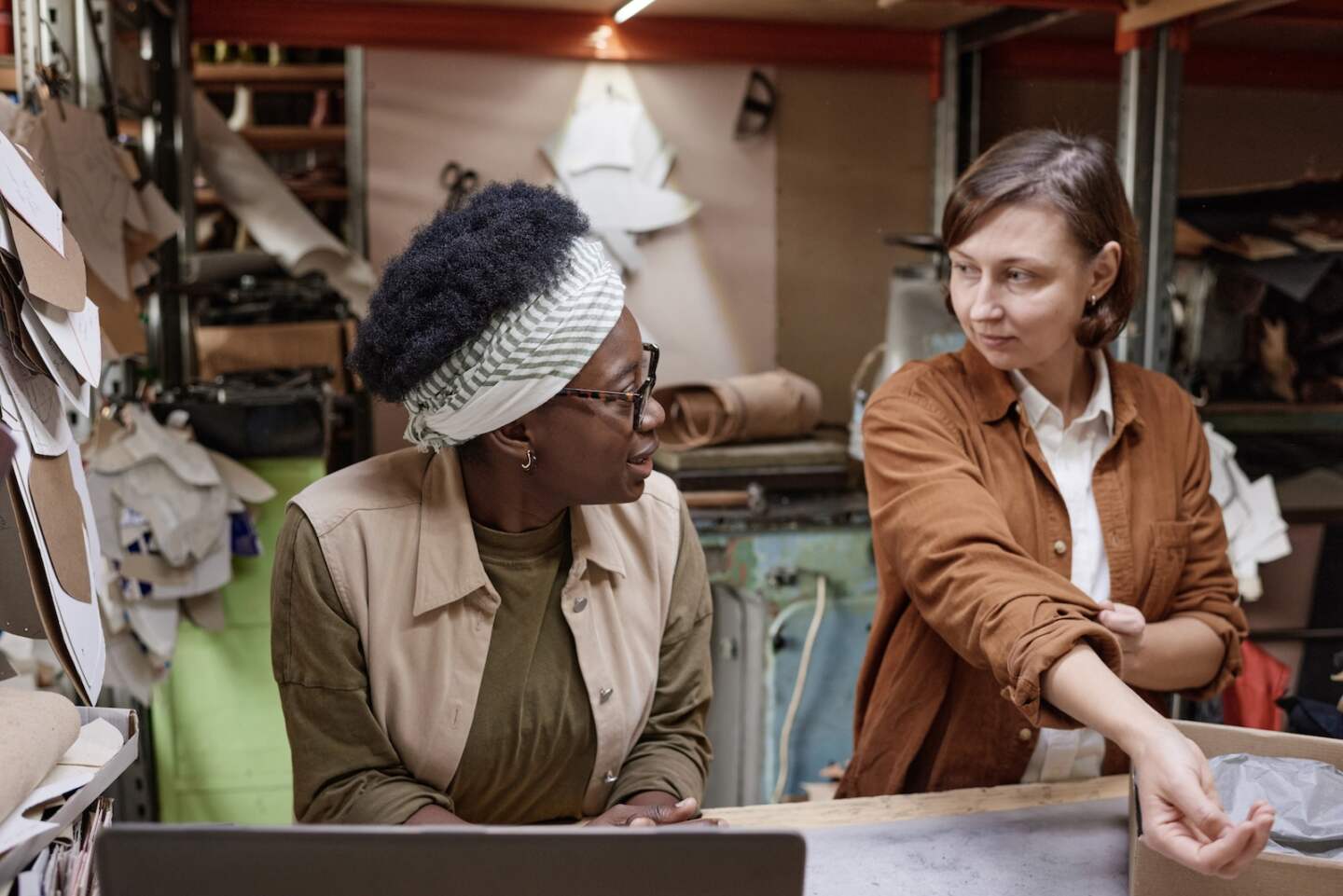 Two colleagues sitting at the table with laptop and discussing work together, they working in the clothes workshop
