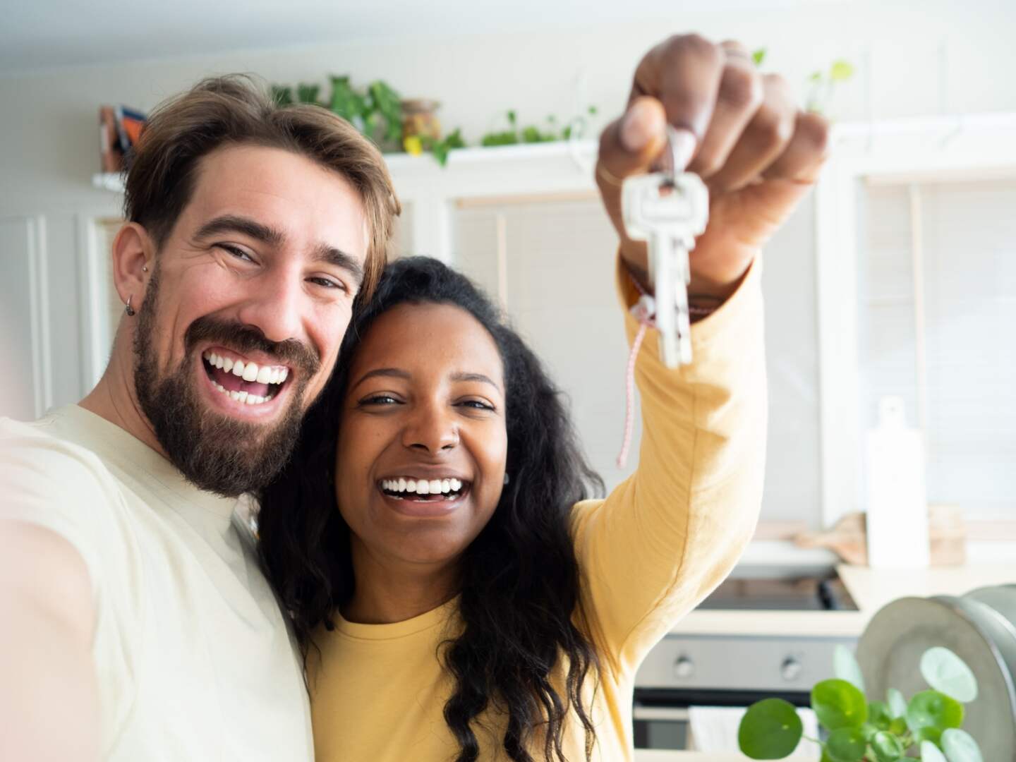 POV selfie of Smiling multiethnic heterosexual couple show the keys to their new house . High quality photo