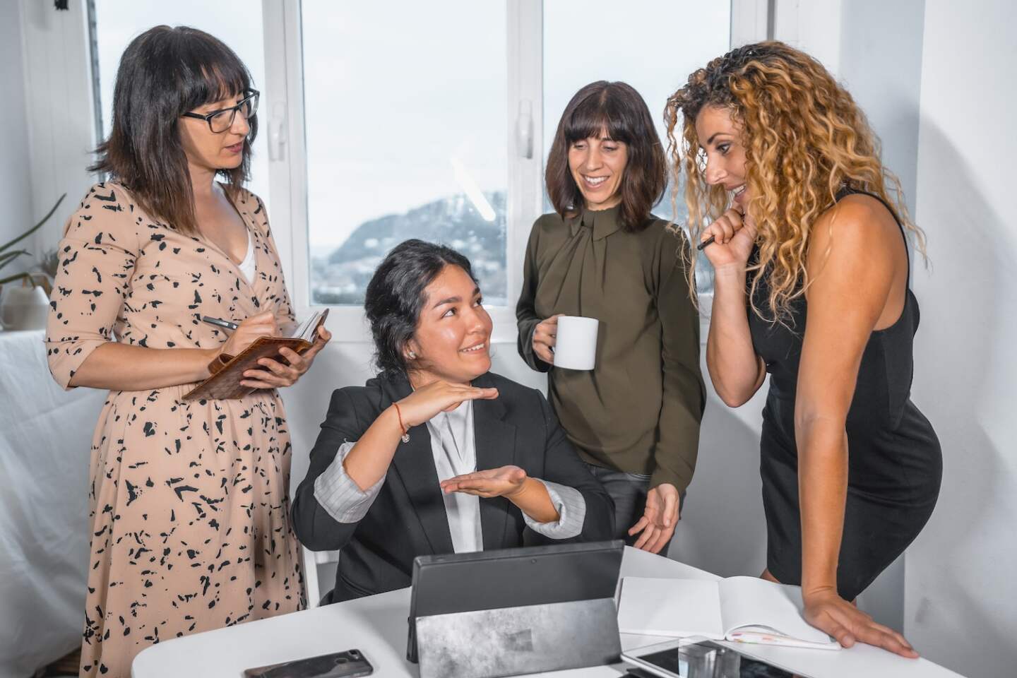 Session young entrepreneurs in the office, head of a Latin ethnic group sitting explaining with work to three young Caucasian women standing next to her...
