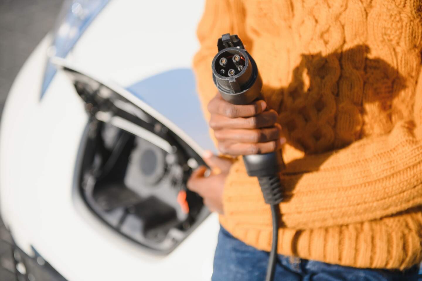 Close up of male hand holding electric charging plug for luxury red car. African businessman charging his auto on station. Eco friendly transport.