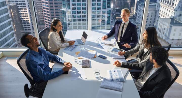 Happy busy international professional business team young people working together in teamwork at group meeting. Multiethnic diverse executives discussing project having fun in office board room.