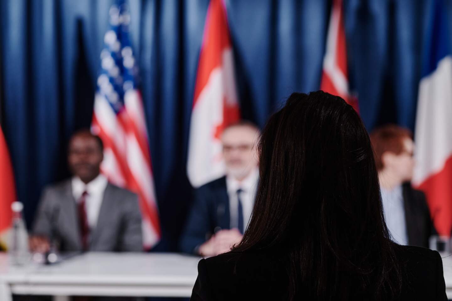 Rear view of female journalist sitting at press conference and listening to politicians