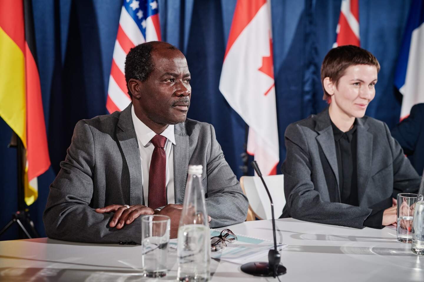 Multiethnic politicians of different countries sitting at table with microphones and bottles of water at business congress
