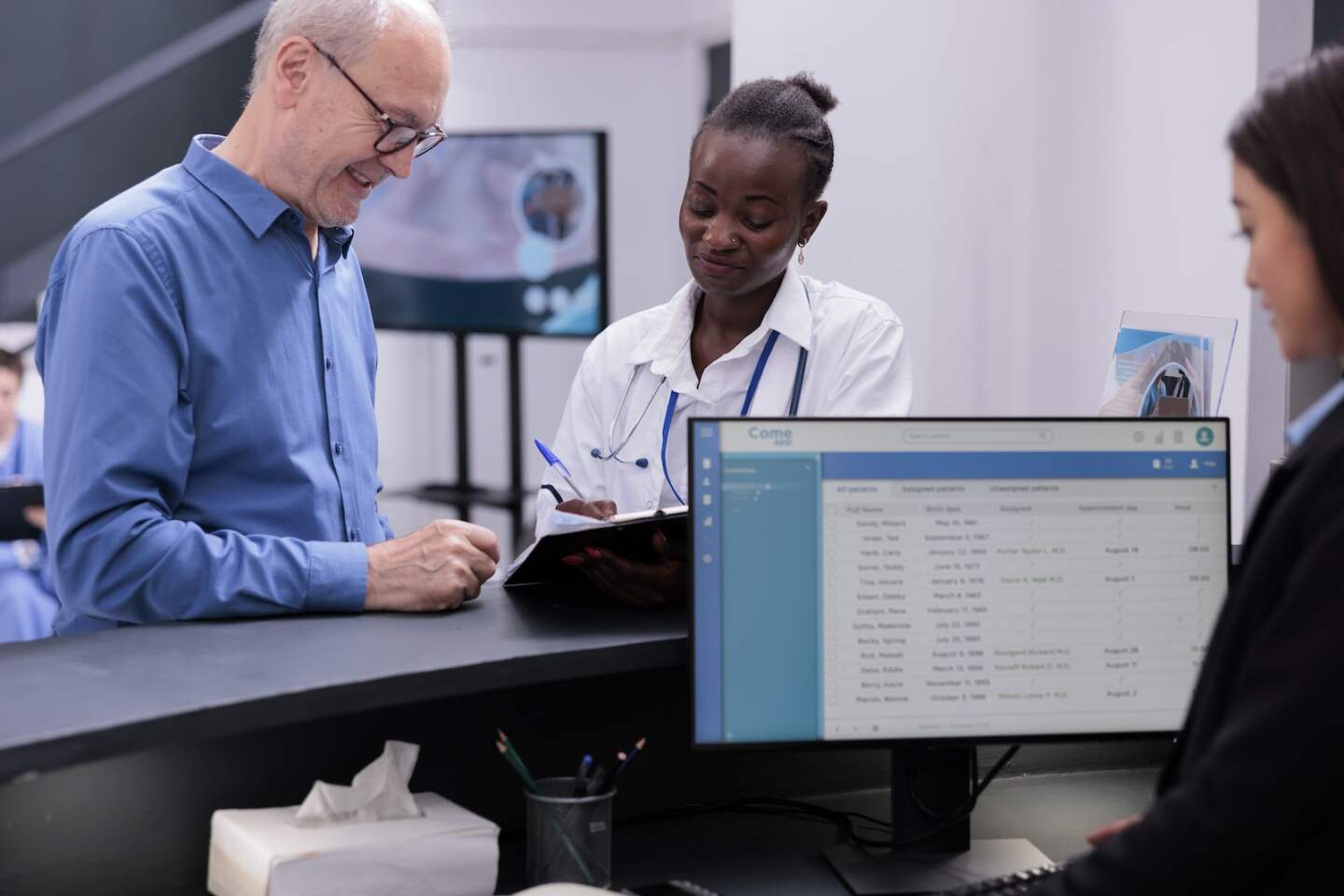 African american doctor showing medical expertise to elderly patient discussing medication treatment in hospital waiting area. Receptionist standing at reception counter checking report on computer