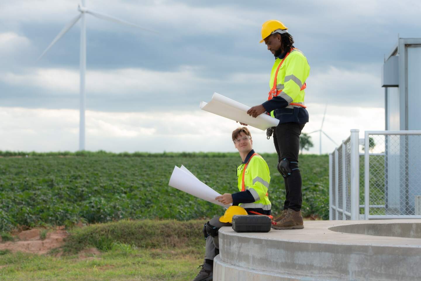 Engineers and technicians work together on the tower base of a large wind turbine with a wind turbine field in the background, The concept of natural energy from wind.