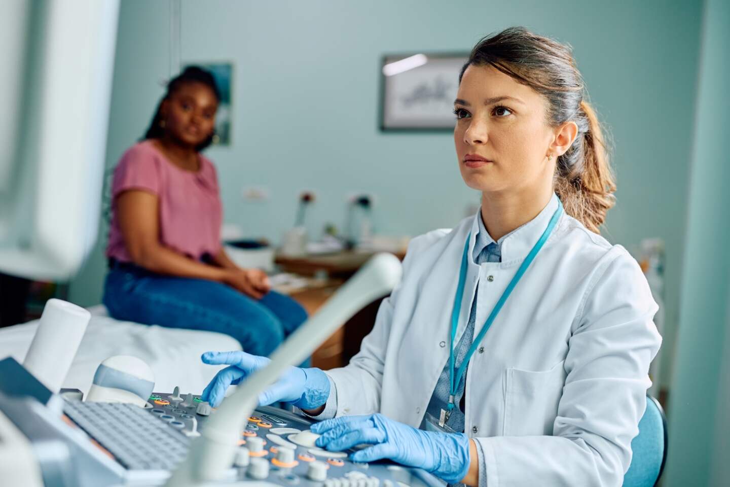 Female gynecologist preparing ultrasound for medical examination of African American woman at the clinic.