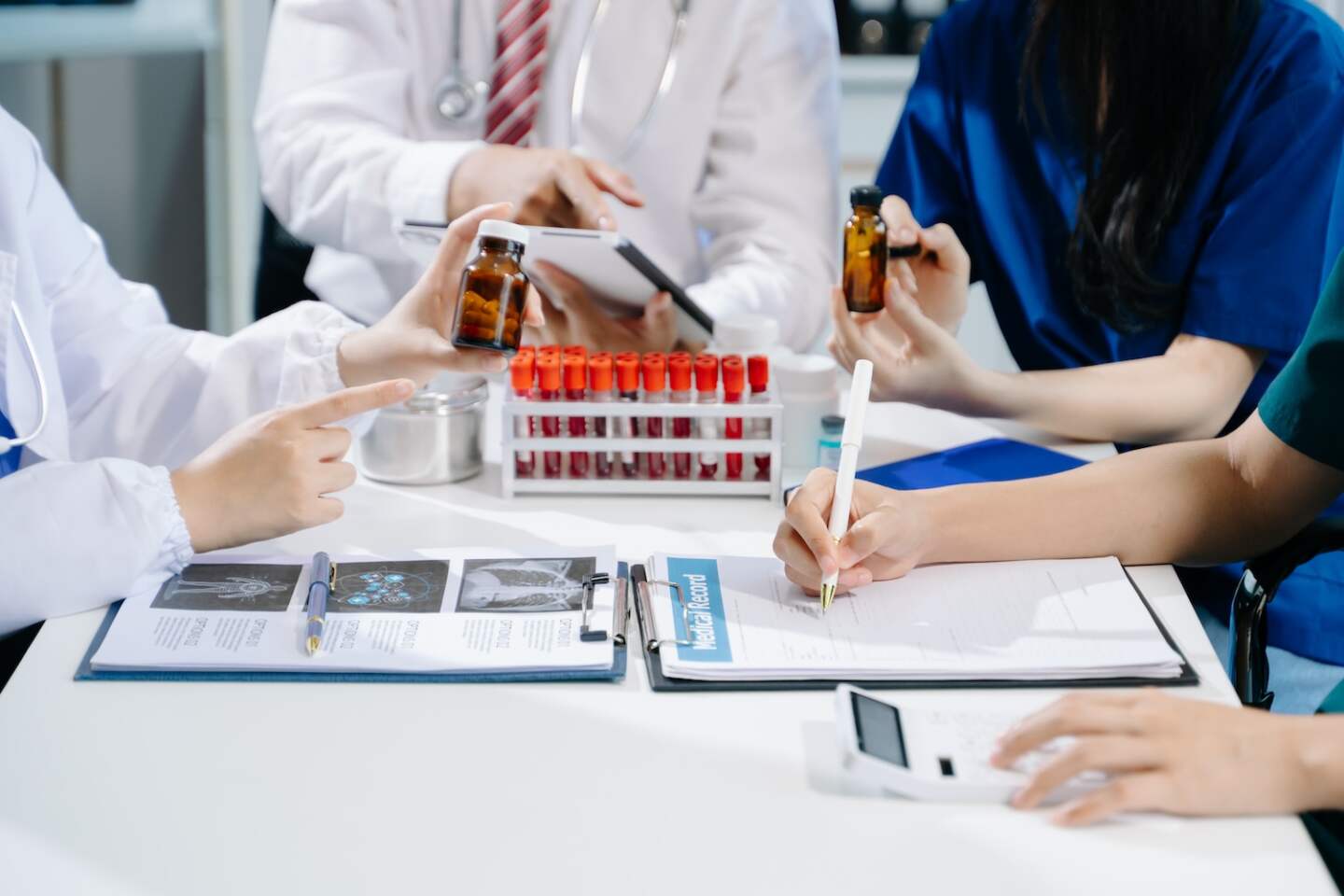 Medical team having a meeting with doctors in white lab coats and surgical scrubs seated at a table discussing a patients working online using computers in the medical industry