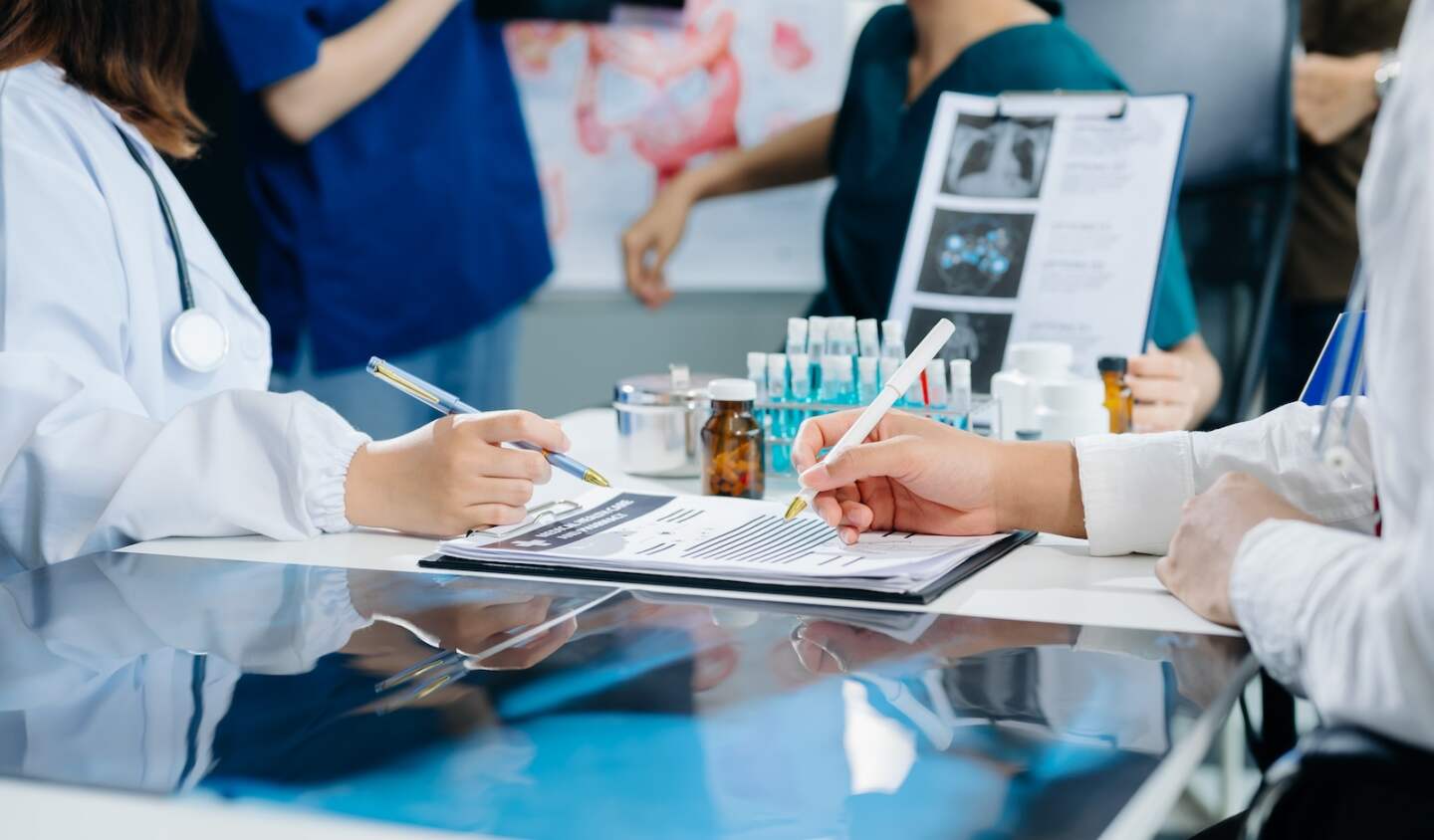 Medical team having a meeting with doctors in white lab coats and surgical scrubs seated at a table discussing a patients working online using computers in the medical industry