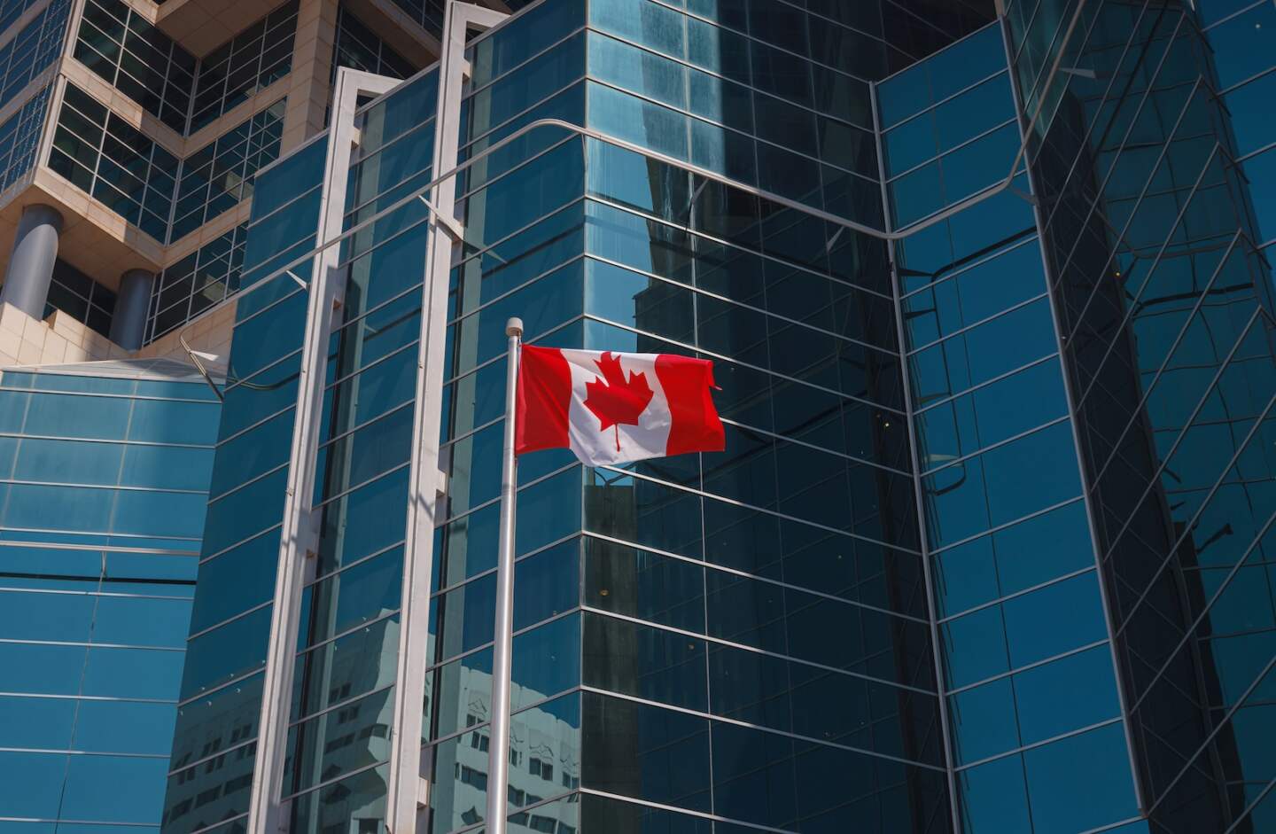Flag of Canada flying against a blue glass skyscraper.
