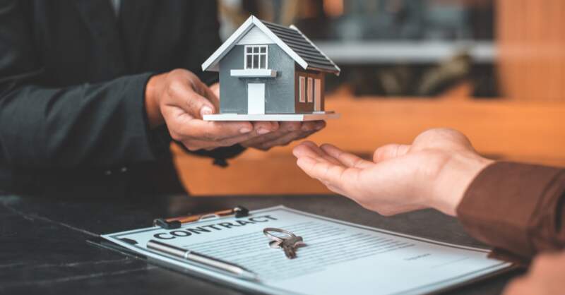 man handing the model of a home to someone over a stack of papers labelled "contract"