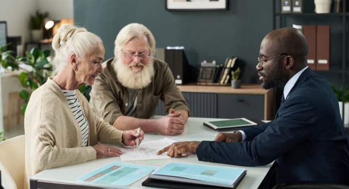 Senior woman signing document while sitting at meeting with financial manager