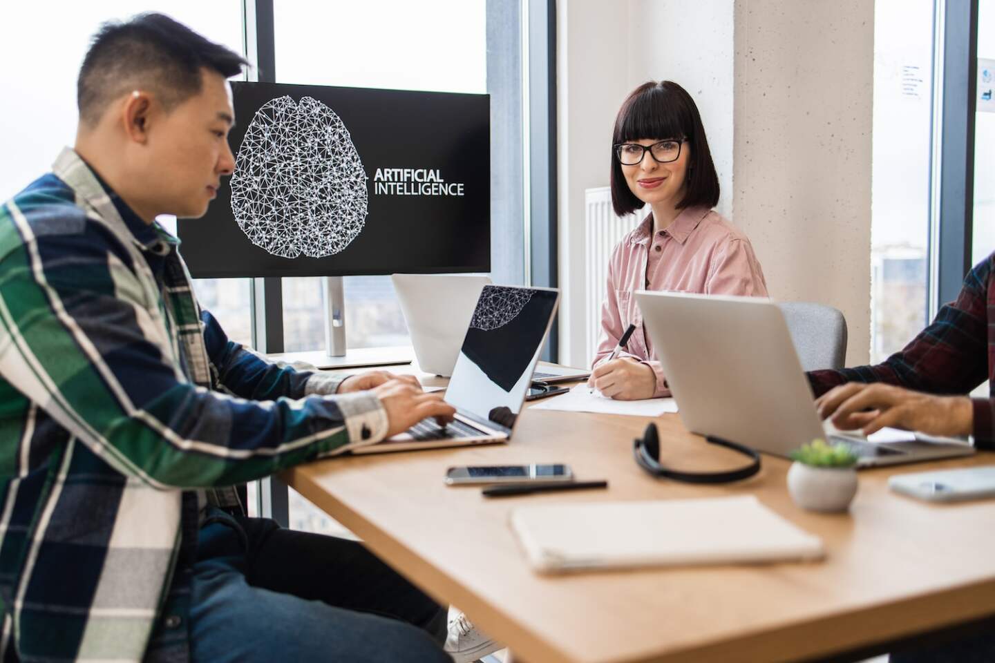 Group of IT experts developing artificial intelligence in modern office setting. Collaborative work environment with laptops and technology on table. Diverse team focused on innovative solutions in AI