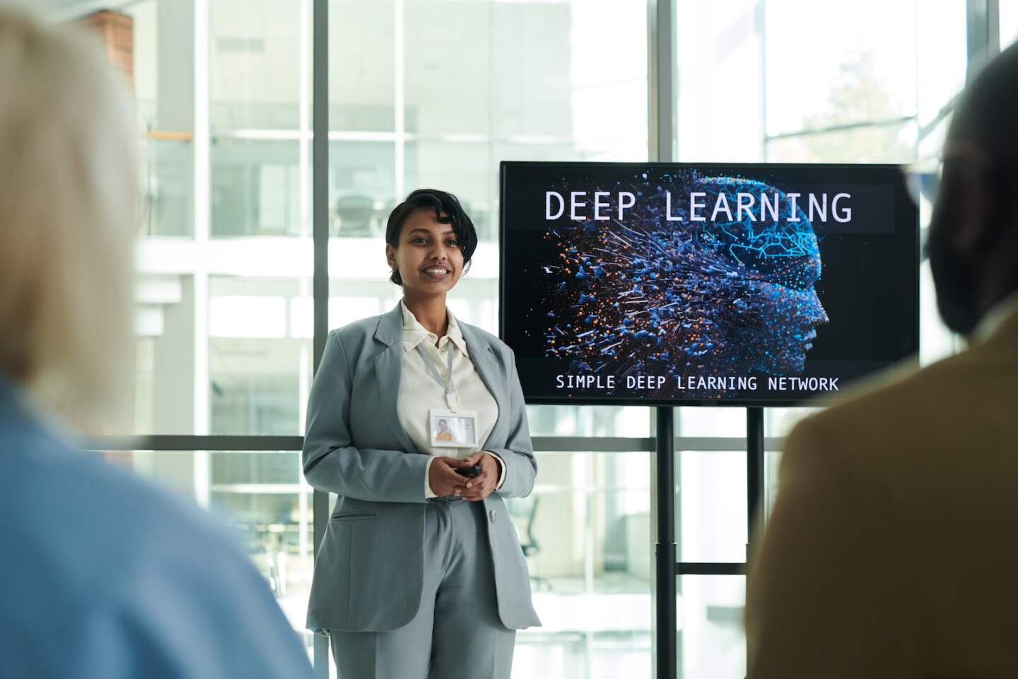 Young smiling female lecturer in formalwear looking at audience while standing by interactive board during presentation at conference