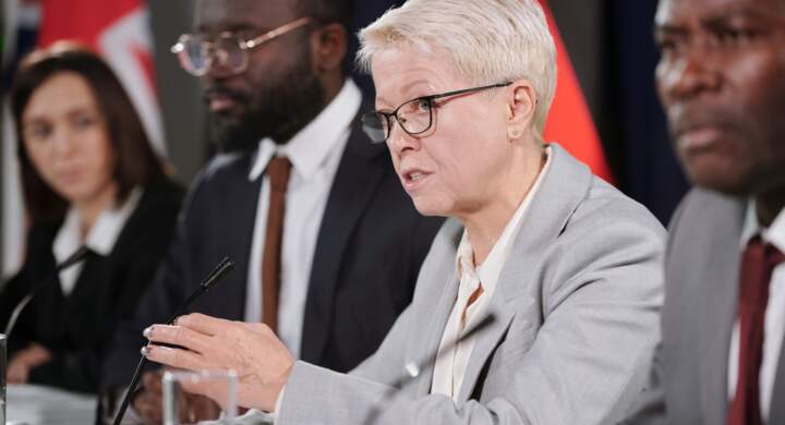 Mature female delegate talking in microphone among foreign colleagues while making political report or answering questions of audience
